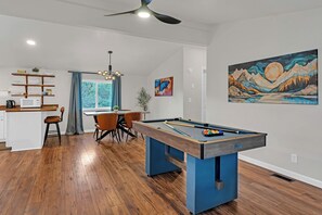 A modern living room with a pool table, a dining area with a table and chairs, a kitchen with a microwave and shelves, and a ceiling fan. - Prvt Grounds: Cozy Yosemite Escape w/ Creek, Billiards, BBQ, Starlink, Pets ok (Mariposa)