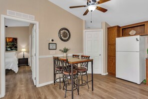 A compact kitchen with a dining table, chairs, a ceiling fan, a refrigerator, and a door leading to another room. - Yosemite Nature Escape: Pvt Gem • Pets • BBQ • Cozy • Split BRs (Mariposa)