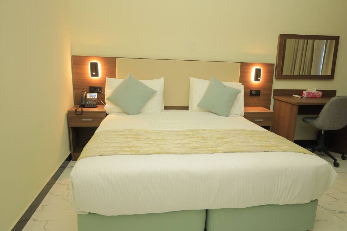 A hotel room with a large bed, two bedside tables with lamps, a desk, and a chair.
