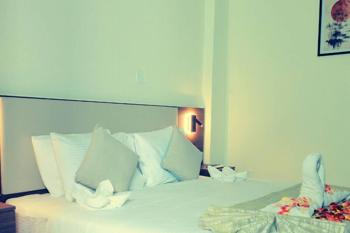 A neatly made bed with pillows, a bedside table, and a wall-mounted light fixture.