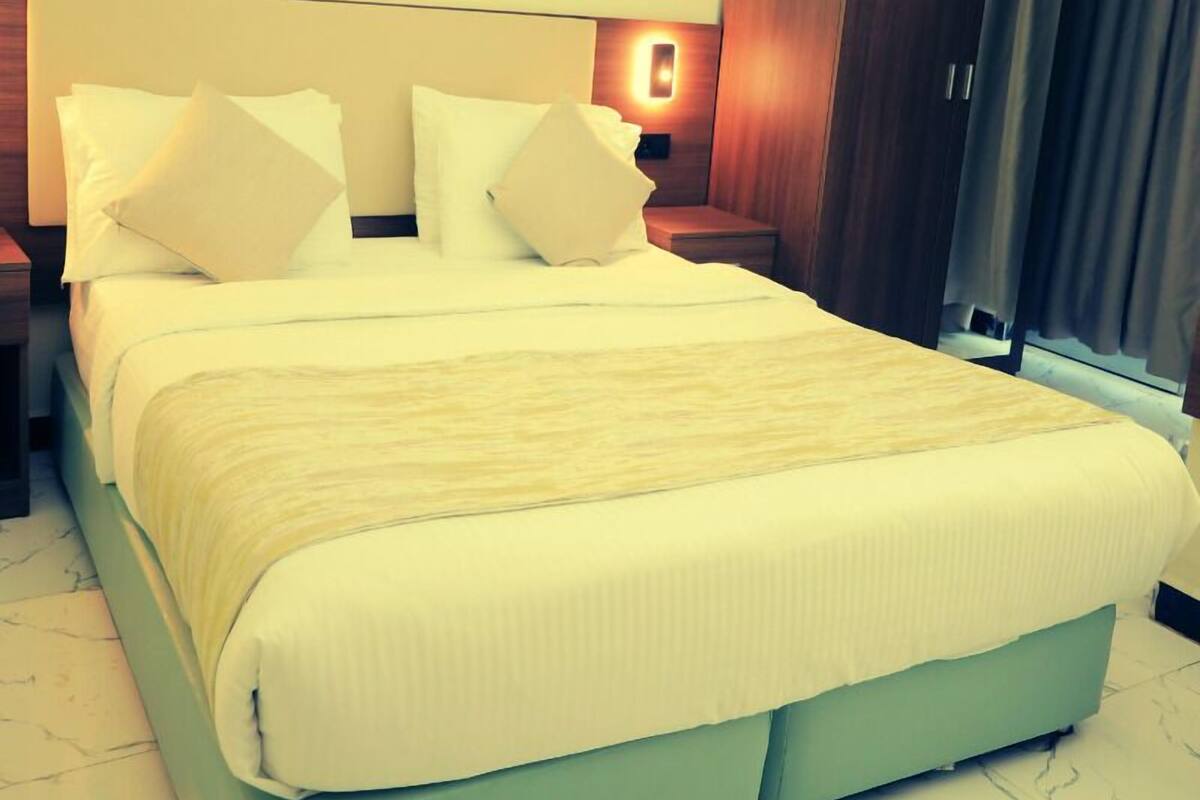 A hotel room with a bed, pillows, a nightstand, a wardrobe, and a window with curtains.