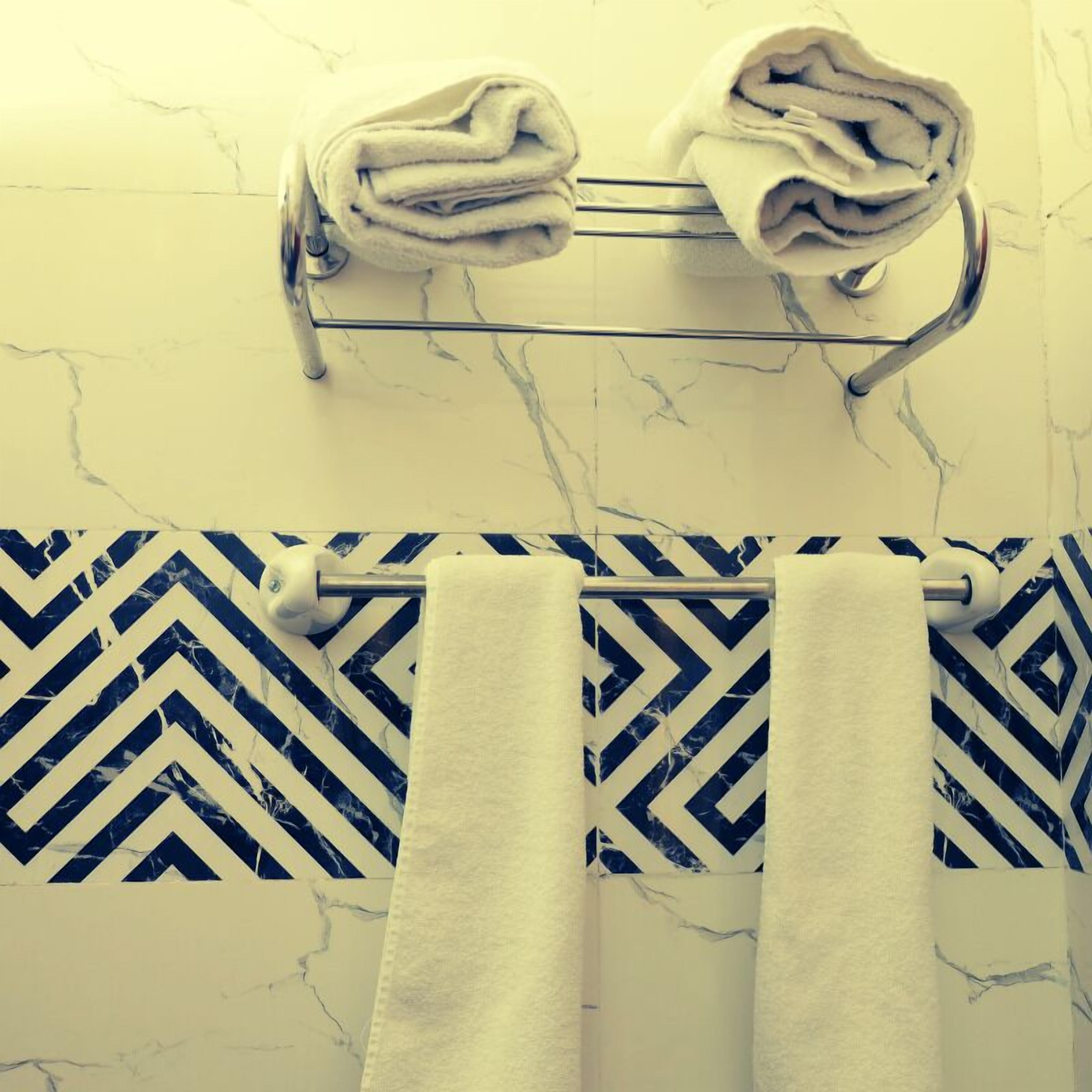 A bathroom with a marble wall, a towel rack with folded towels, and a patterned tile backsplash.