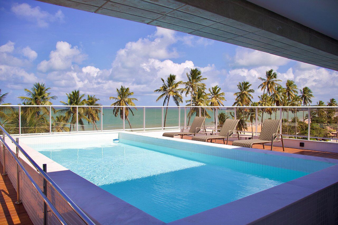 A rooftop infinity pool with a view of the ocean and palm trees.