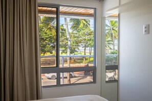 Ein Zimmer mit großem Fenster mit Blick auf eine Straße, gesäumt von parkenden Fahrzeugen und Palmen.