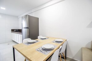 A modern kitchen with white cabinets, a stainless steel refrigerator, and a dining table set for four. - Puerto Ventura - Beachfront Apartment by Carpediem (João Pessoa)