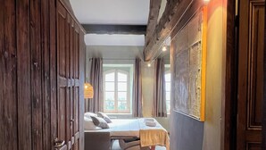 Ein schmaler Flur führt zu einem Schlafzimmer mit einem Bett, einem Holzschrank und einem Fenster mit Vorhängen.