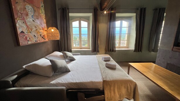 Ein Hotelzimmer mit einem Bett, zwei Nachttischen, einem Schreibtisch und einem großen Fenster mit Blick ins Freie.