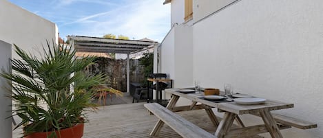 Un terrazzo in legno con tavolo e sedie da picnic, una pianta in vaso e vista su un edificio sullo sfondo.