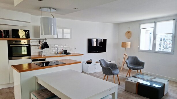 A modern kitchen with a built-in oven, microwave, and sink. There is a dining area with a white table and chairs, and a TV mounted on the wall. - Beach Apartment 100m from the Sea (La Tranche-sur-Mer)