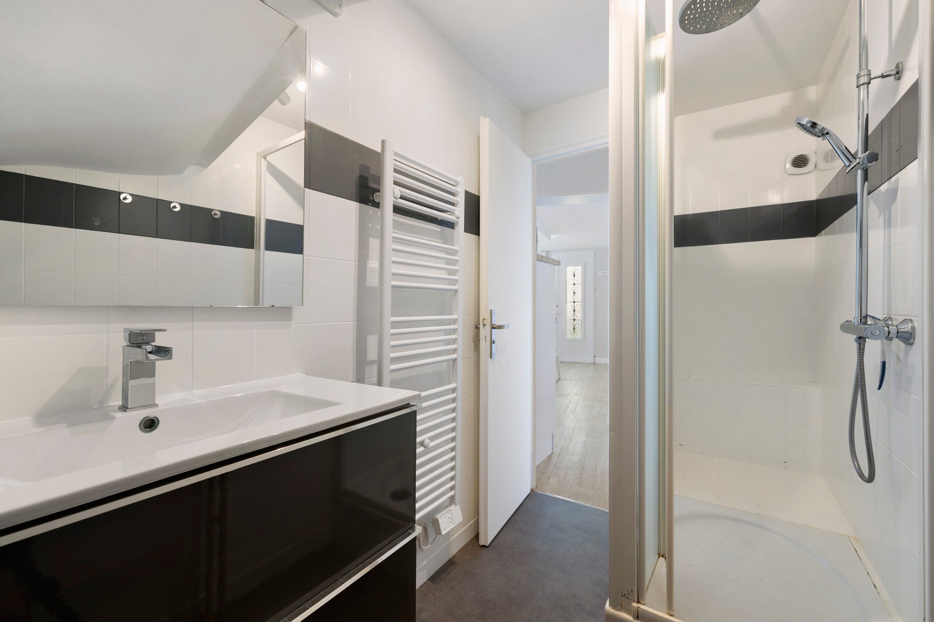 A modern bathroom with a white sink, a glass-enclosed shower, and a towel rack.
