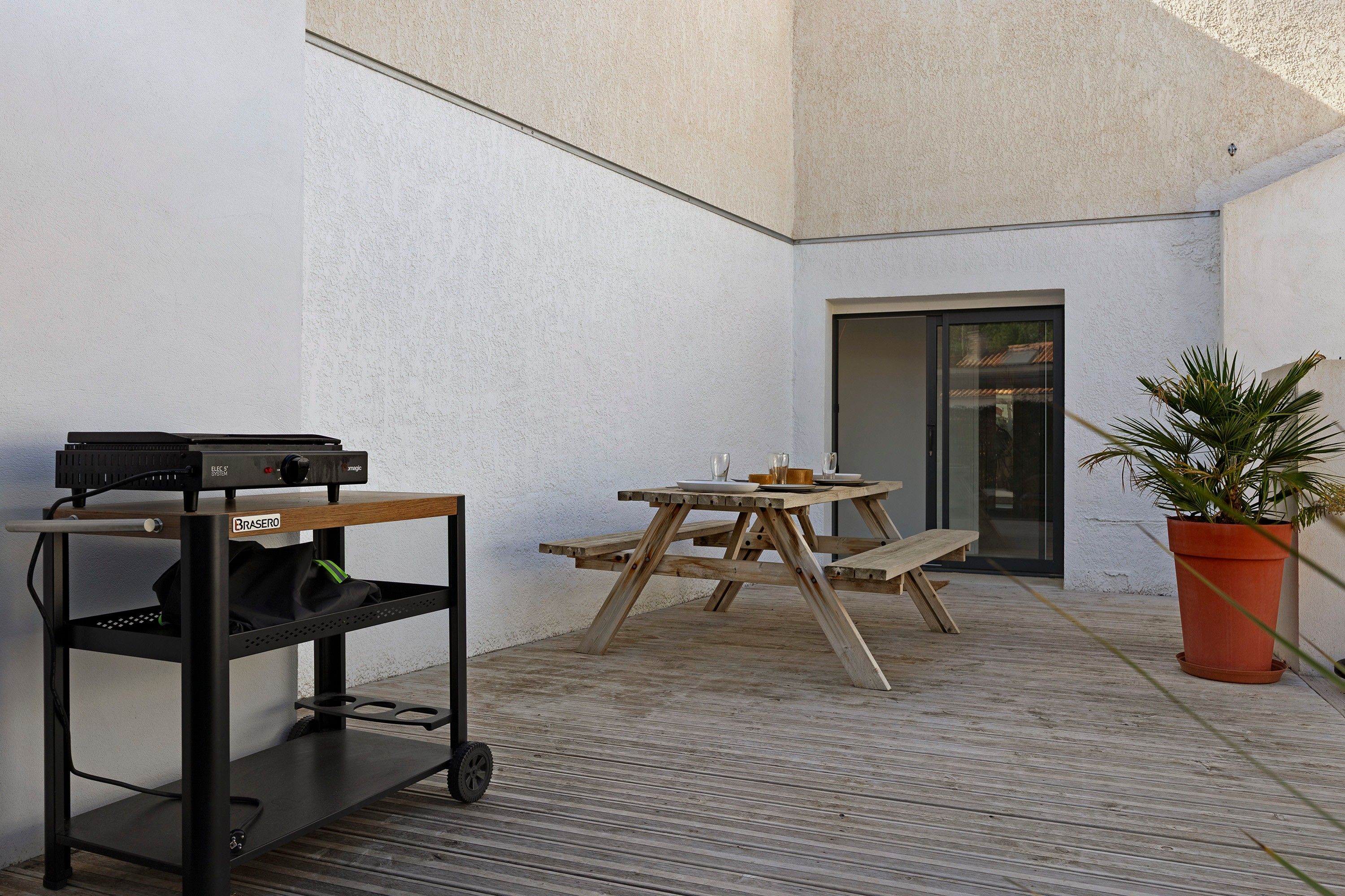 Eine Terrasse mit Tisch und Stühlen, ein Wagen mit elektronischer Ausrüstung und ein Blumentopf.