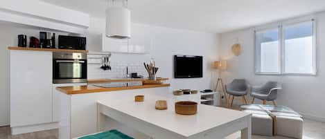 A modern kitchen with a central island, built-in appliances, and a dining area with a glass table and teal cushions.