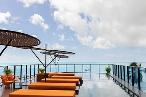 A rooftop infinity pool with orange lounge chairs and umbrellas, overlooking the ocean. - Setai Edition #113 - Seaside by Carpediem (João Pessoa)