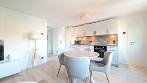 A modern kitchen with white cabinets, a round wooden table, and two grey upholstered chairs. - Berth 6 - close to the beach and modern (Timmendorfer Strand)