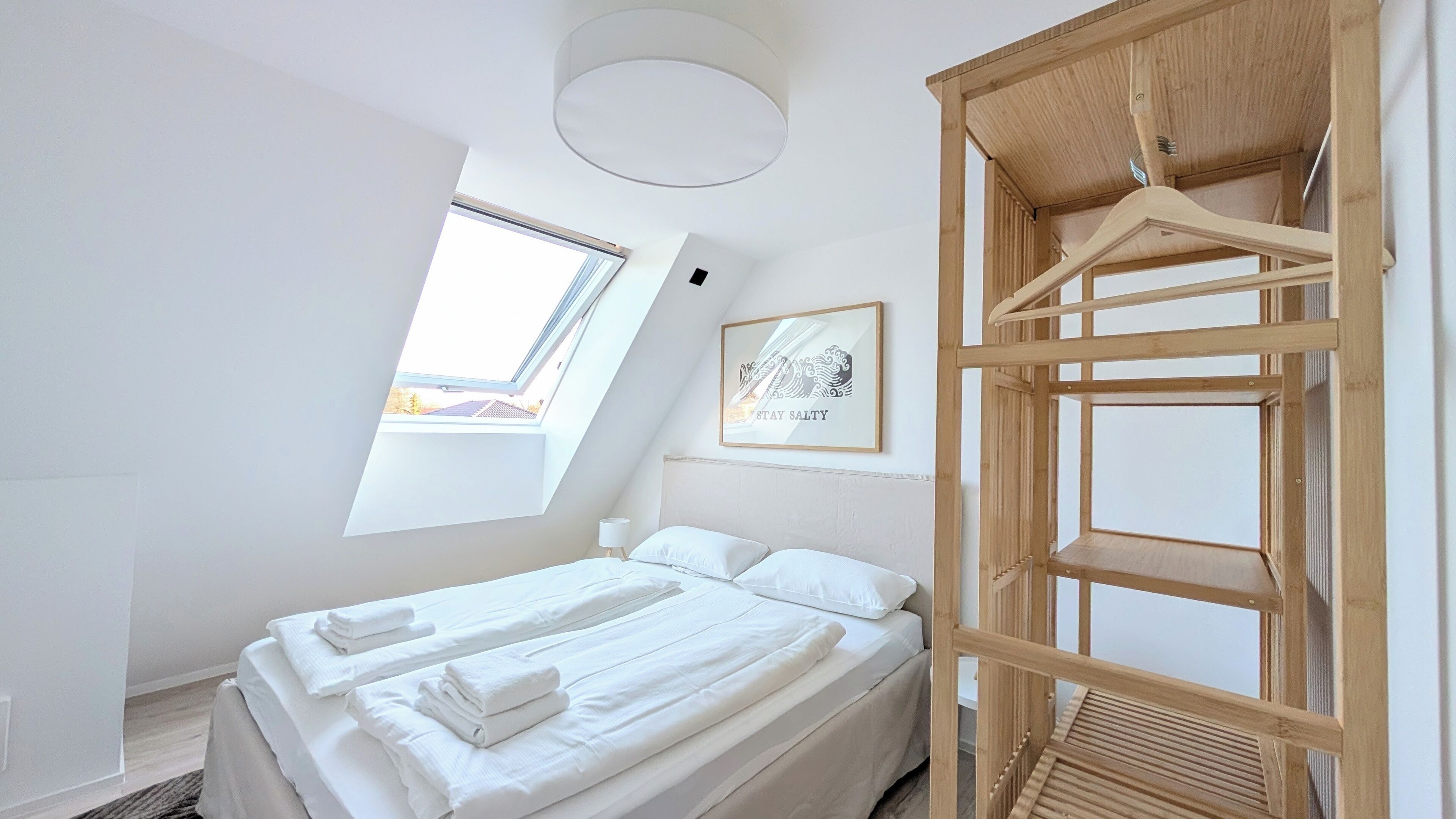 A modern bedroom with a bed, a wooden wardrobe, a skylight, and a framed artwork.