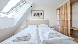 A modern bedroom with a sloped ceiling, two beds, a wooden wardrobe, and a framed artwork on the wall. - Berth 6 - close to the beach and modern (Timmendorfer Strand)