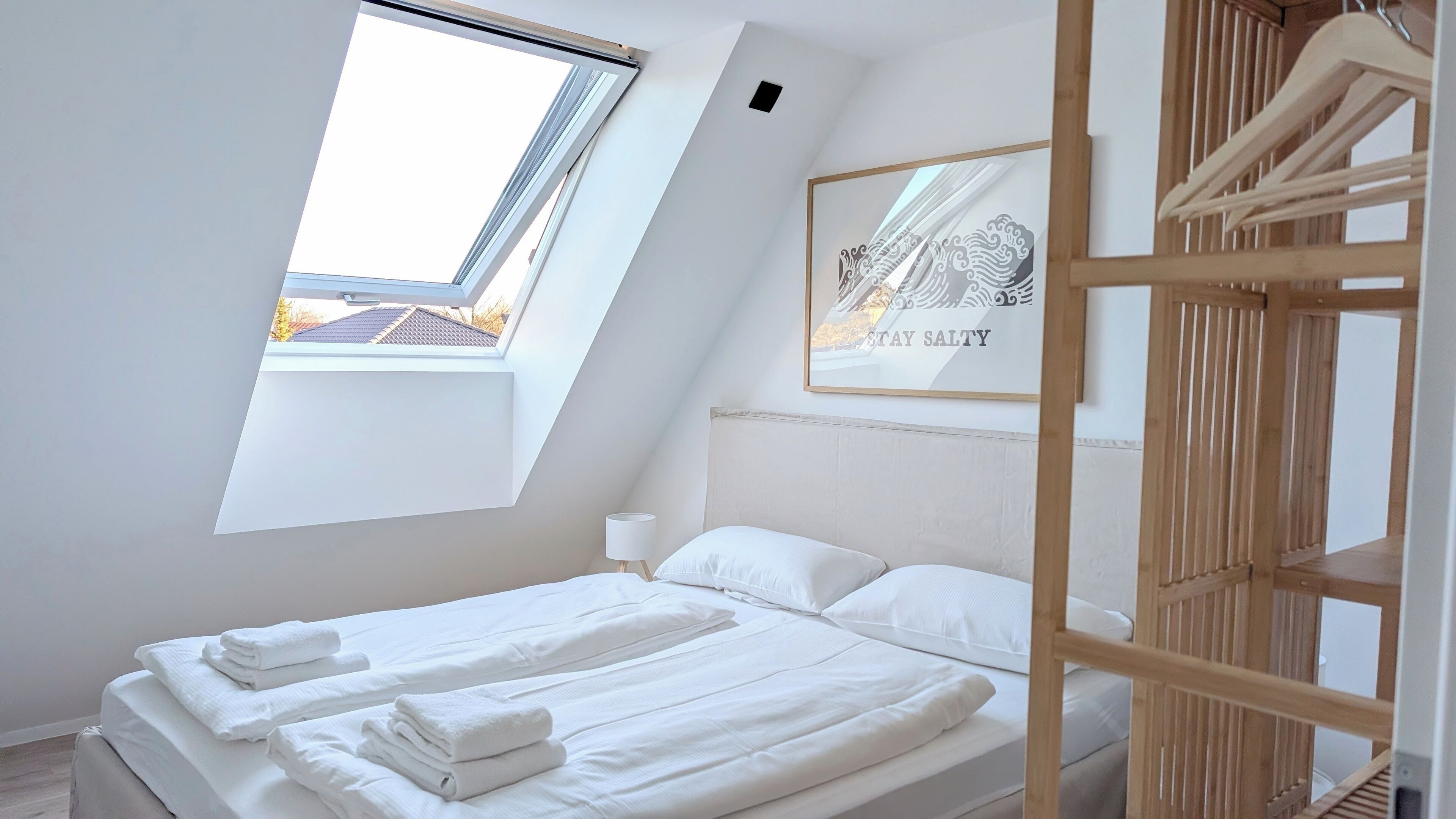 A bedroom with a skylight, a bed with neatly folded towels, a bedside lamp, and a framed artwork on the wall.
