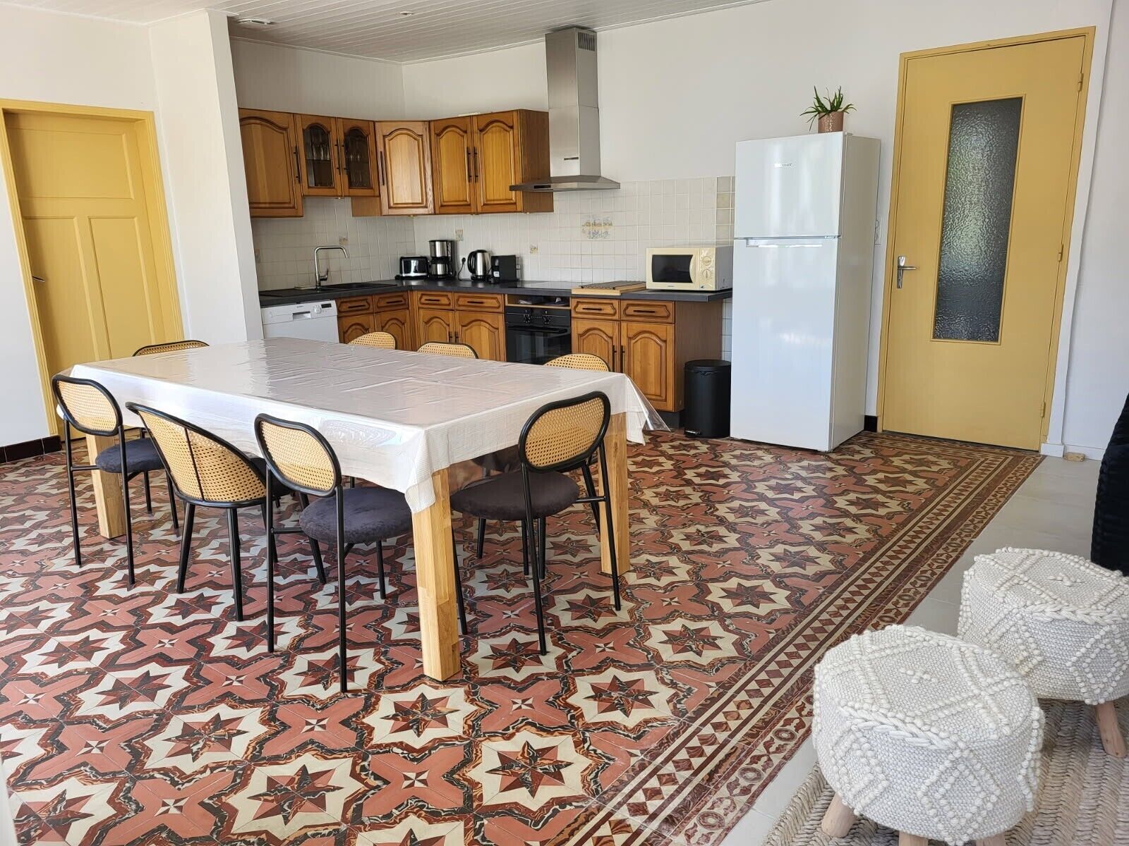 Une cuisine avec des meubles de rangement en bois, une table à manger avec des chaises, un réfrigérateur et un sol à motifs.