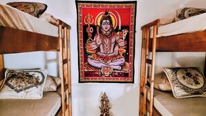 A room with two bunk beds, a small table with a statue, and a tapestry with a religious figure. - Vila Urban Hostel - Jardins (São Paulo)