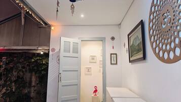 Un couloir avec une porte blanche, une petite table ornée d’un flamant rose rouge, et un mur décoré de tableaux encadrés et d’une découpe circulaire.