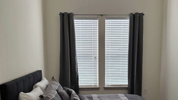A bedroom with a bed, a small side table, and a window with blinds. - Luxury 2 bedroom with two baths Pool Gym (Frisco)