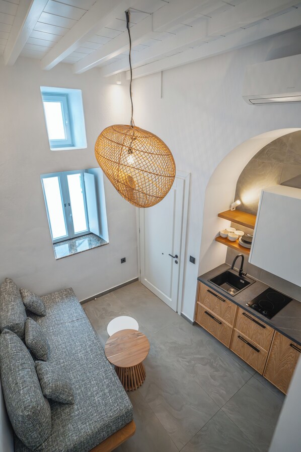 Een compacte keuken met een inbouwoven, een hanglamp en een klein eethoekje met een ronde tafel en kussens.
