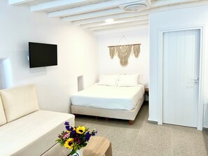 Un dormitorio con cama, televisor montado en la pared, un tapiz de macramé y una puerta blanca.