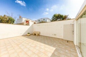 Une terrasse couverte avec un sol carrelé, un banc et une porte vitrée donnant accès à un espace douche.