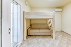 Un lit superposé avec un espace salon au niveau inférieur, une porte-fenêtre coulissante et un sol carrelé.