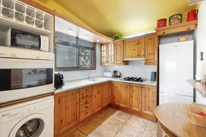 Een kleine keuken met houten keukenkastjes, een inbouwoven, een wasmachine en een koelkast.