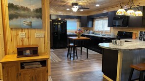 A modern kitchen with wooden paneling, a central island, and a painting of a lake scene. - Peaceful 3-bedroom cabin with AC in charming Danbury with Lake 26 access (Danbury)