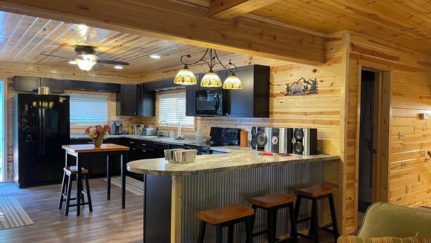 A modern kitchen with wooden beams, a central island with stools, a refrigerator, and a microwave. - Peaceful 3-bedroom cabin with AC in charming Danbury with Lake 26 access (Danbury)