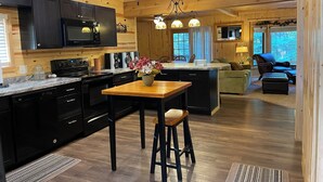 A modern kitchen with black cabinets, a wooden island, and a dining area with a table and bar stools. - Peaceful 3-bedroom cabin with AC in charming Danbury with Lake 26 access (Danbury)