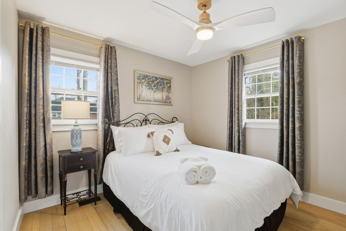 A bedroom with a bed, a nightstand, a ceiling fan, and curtains.