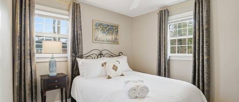 A bedroom with a bed, a nightstand, a ceiling fan, and curtains.