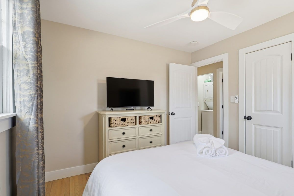 Une chambre à coucher avec un lit, un téléviseur posé sur une commode et une porte donnant sur une autre pièce.