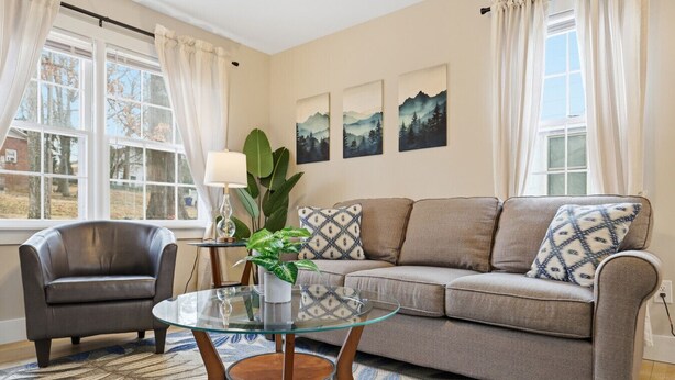 Un salon comprenant un canapé, un fauteuil, une table basse en verre et une grande plante.