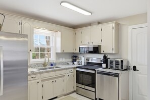 Cocina con armarios blancos, electrodomésticos de acero inoxidable, una ventana y una puerta.