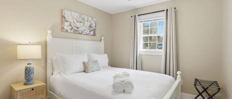 A bedroom with a bed, a nightstand, a lamp, a ceiling fan, a window with curtains, and a wall-mounted artwork.