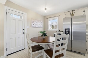 Una cocina con un refrigerador de acero inoxidable, una mesa de comedor con sillas, una planta en maceta y una ventana con vistas.