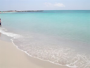 Ein Strand mit klarem türkisblauem Wasser, einem sandigen Ufer und einer in der Ferne liegenden Felsformation.