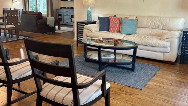 A living room with a beige sofa, a glass coffee table, and striped chairs. - Three Blocks to Flagler - Fenced Backyard Pets OK (New Smyrna Beach)