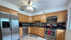 A kitchen with wooden cabinets, a stainless steel refrigerator, a dishwasher, a stove, and a ceiling fan. - Three Blocks to Flagler - Fenced Backyard Pets OK (New Smyrna Beach)