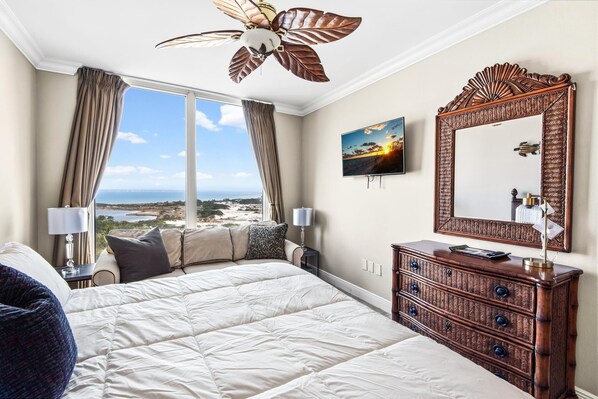 A hotel room with a large bed, a wooden dresser, a ceiling fan, a large window with a view, and a wall-mounted TV. - Portofino Island Resort 4-1101 (Pensacola Beach)