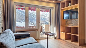 Een moderne woonkamer met een bank, een televisie op een houten plank en een groot raam met uitzicht op besneeuwde bergen.