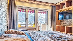 Een slaapkamer met een bed, een televisie, een houten plank en een raam met gordijnen.