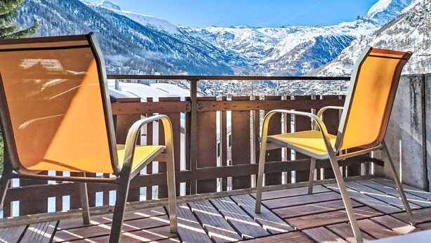 Een houten terras met twee gele stoelen, gericht op een besneeuwd berglandschap.