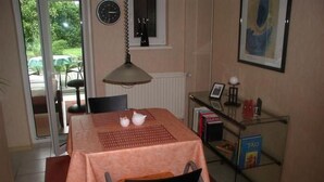 En matplats med ett bord dukat för två personer, en stol, ett element, en klocka, en inramad tavla och en glashylla med böcker och en lampa.