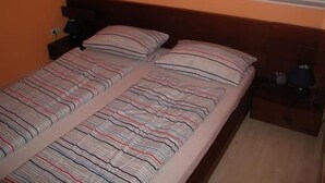 A double bed with striped bedding, two pillows, a nightstand with a lamp, and two windows with blinds. - Appartement in Spekendorf mit Terrasse by Interhome (Aurich)