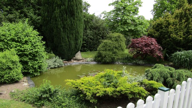 A garden with a pond, various trees, and a white picket fence. - Appartement in Spekendorf mit Terrasse by Interhome (Aurich)